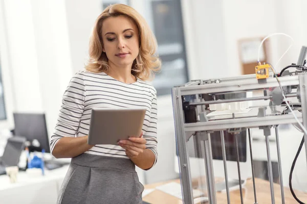 Schöne Frau, die ihr Tablet benutzt, während der 3D-Drucker arbeitet — Stockfoto