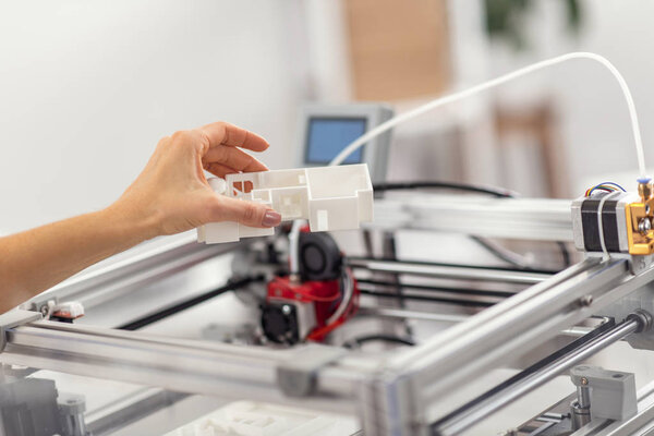 Female hand holding a house model above 3D printer