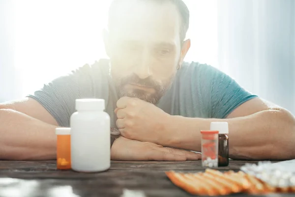 Pensativo homem sério sentado e com vista para os medicamentos . — Fotografia de Stock