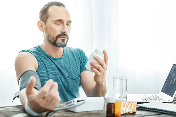 Hombre barbudo infeliz midiendo el pulso sosteniendo el frasco . — Foto de Stock