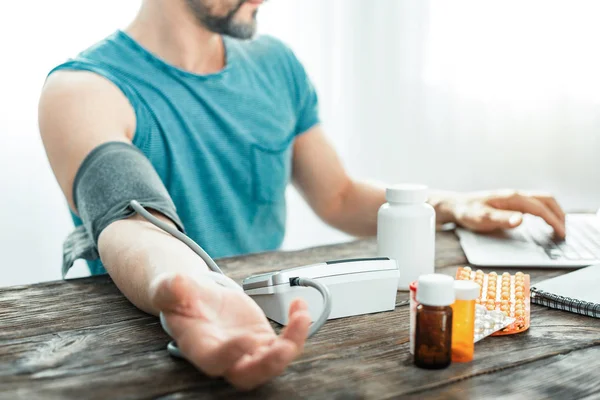 Hombre ocupado atento midiendo el pulso y usando el portátil . — Foto de Stock