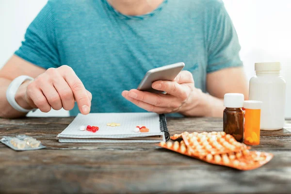 Concentrated attentive man pointing at pills holding the cellphone. — Stock Photo, Image