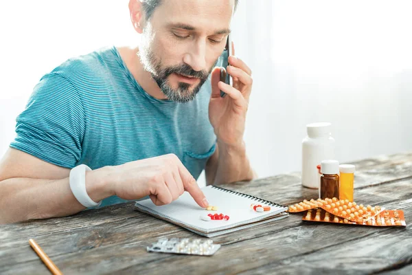 Pleasant interested man having conversation and pointing at pills.