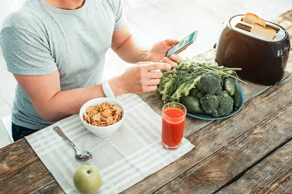 Attentive responsible man having breakfast and using the smartphone. — Stock Photo, Image