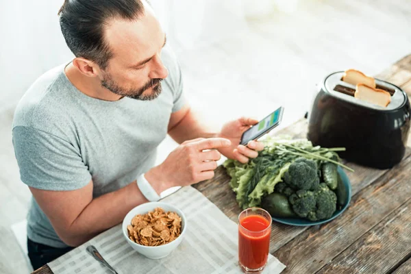 Концентрований обережний чоловік використовує свій мобільний телефон, який готується до їжі . — стокове фото