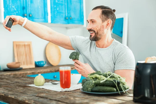 Pleasant happy man holding a broccoli and making selfie. — Stock Photo, Image