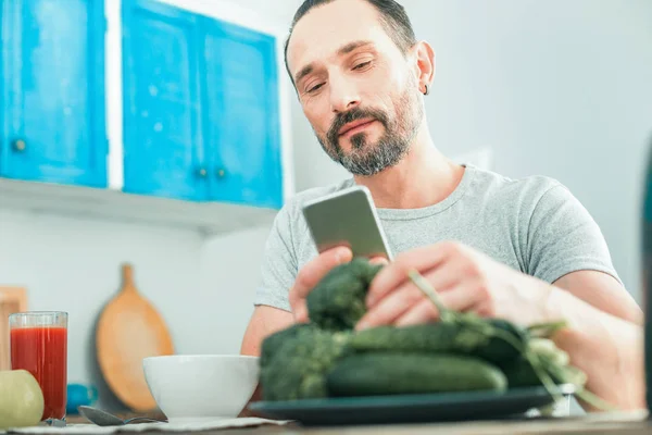 Nöjd smart människa tar grönsaker och använder mobilen. — Stockfoto