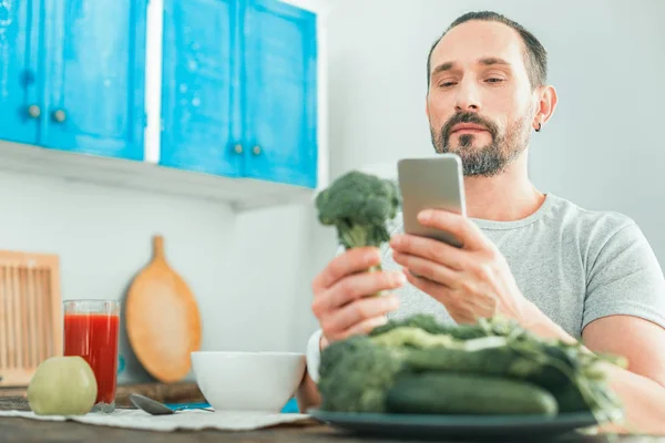 Lugn koncentrerade man tittar på mobilen håller en broccoli. — Stockfoto