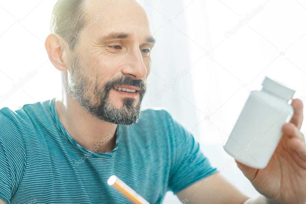 Pleasant handsome man smiling and looking at the jar.