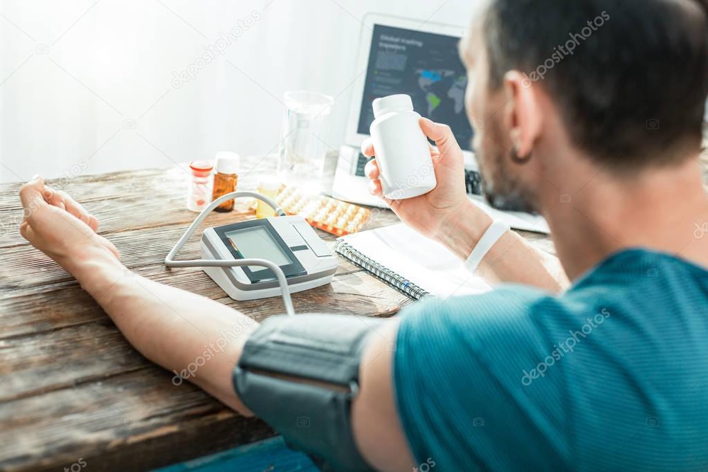 Busy focused man holding a jar and measuring pulse.