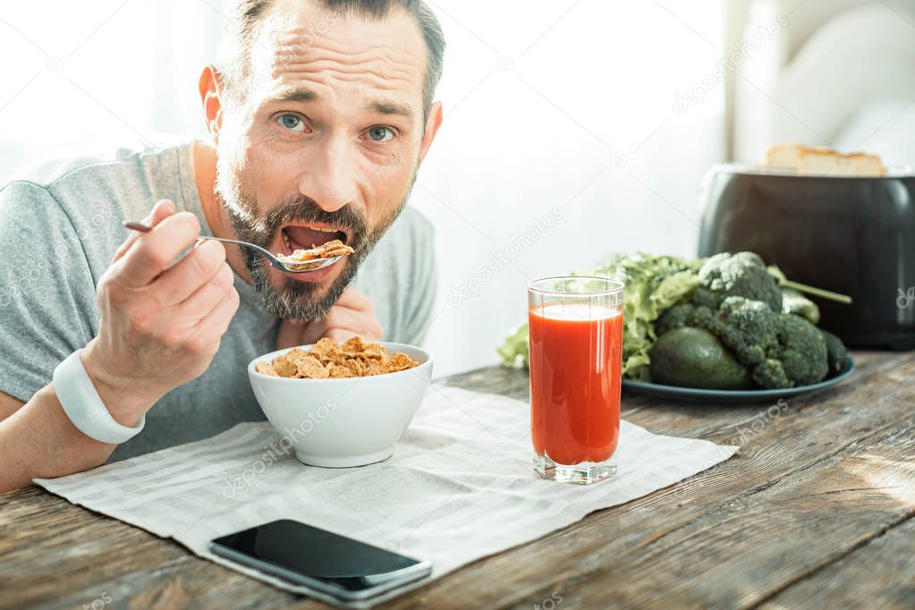 Handsome pleasant man holding a spoon and eating flakes.