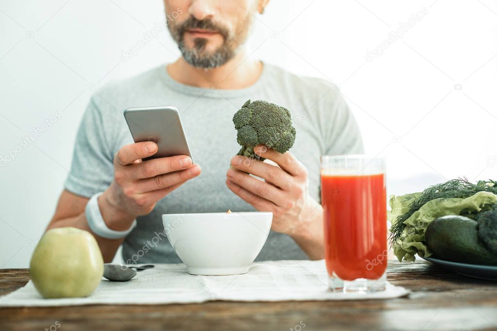 Interested busy man siting and holding a broccoli.
