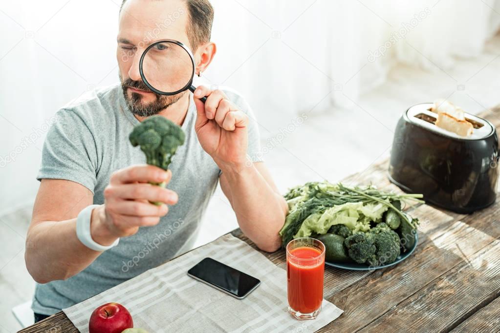 Occupied curious man sitting and examining a broccoli.