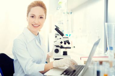 Mikroskop, dizüstü bilgisayarda çalışan araştırmacı gülen.