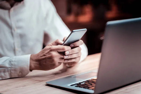 Obsazené vážný muž pomocí notebooku a drží jeho smartphone. — Stock fotografie