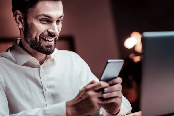 Agradable hombre sonriente sosteniendo el teléfono celular y regocijándose . —  Fotos de Stock