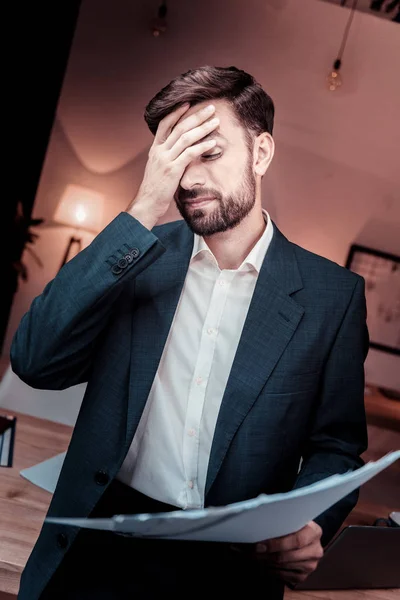 Ongelukkige uitgeput man aan te raken aan het hoofd en houden van documenten. — Stockfoto