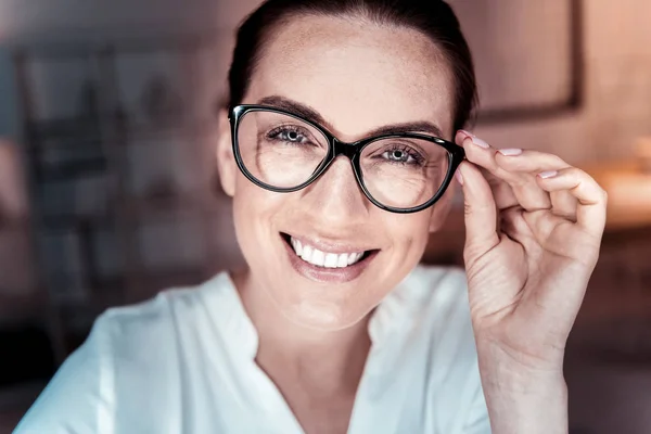 Satisfied pleasant woman supporting her glasses and smiling. — Stock Photo, Image