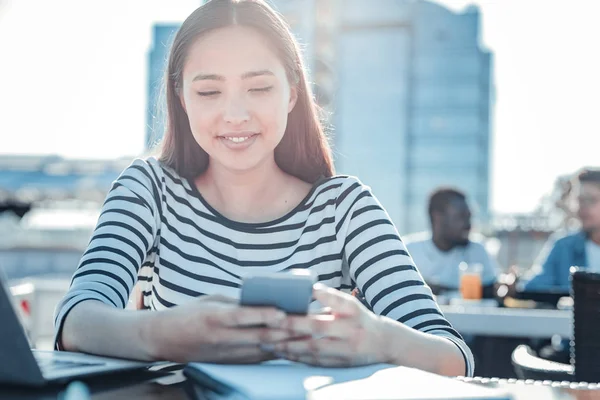 Chica radiante sentada a la luz del sol y usando su teléfono — Foto de Stock