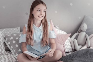 Gülümseyen kız yatakta otururken bir kitap tutan