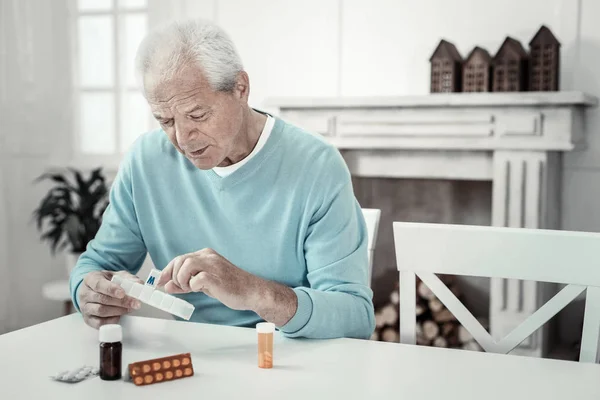 Hombre interesado envejecido sosteniendo paquete de tabletas y con vistas a ella . — Foto de Stock