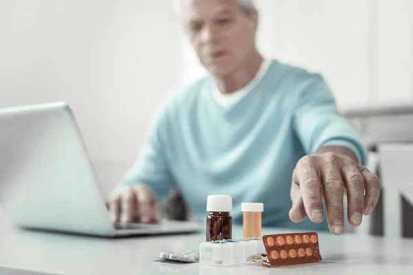 Aged senior man sitting and holding hand near pills. — Stock Photo, Image