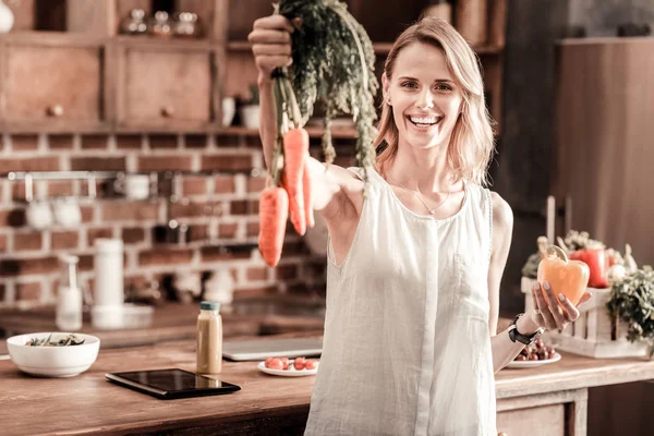 Mujer positiva deleitada sosteniendo zanahorias —  Fotos de Stock