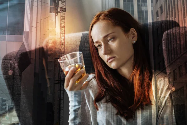 Exhausted depressed woman sitting alone and looking at the glass of alcohol