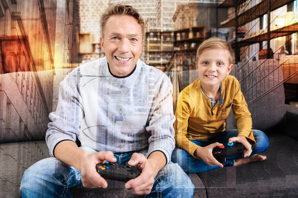 Feliz padre sonriendo mientras juega videojuegos con su hijo alegre —  Fotos de Stock