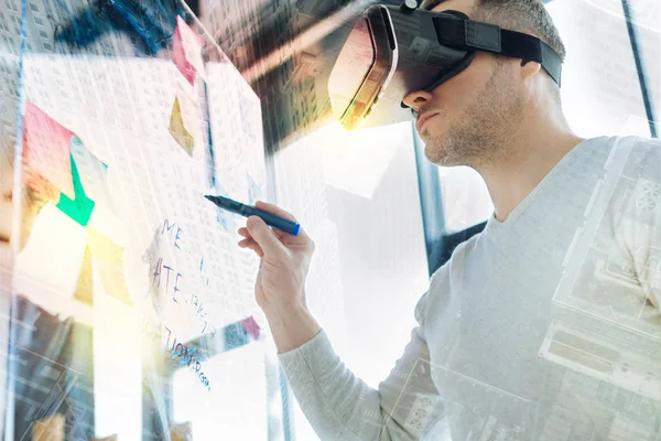 Attentive man in virtual reality glasses looking serious while holding a marker