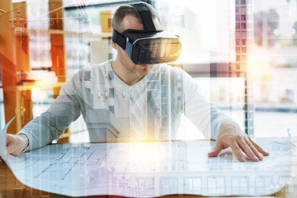 Arquitecto inteligente sentado con un dibujo mientras usa gafas de realidad virtual —  Fotos de Stock