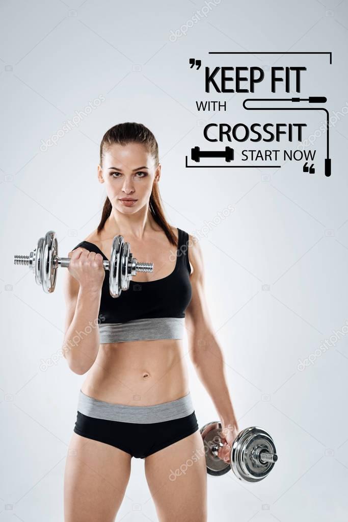 Strong sportswoman looking calm while holding big hand weights