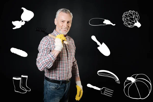 Hombre alegre sonriendo mientras está de pie con rastrillos en la mano — Foto de Stock