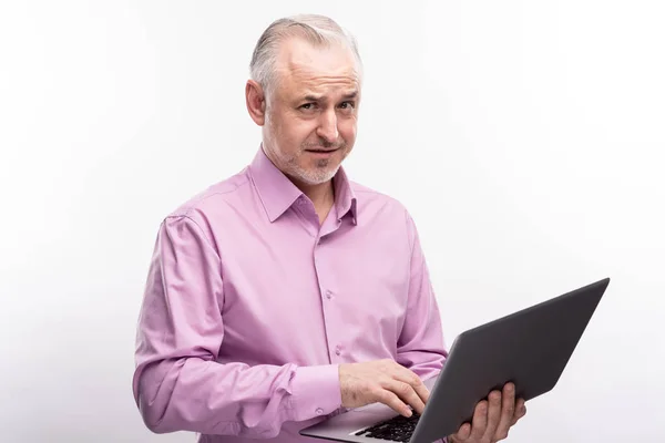 Uomo dai capelli grigi accigliato e in posa con il computer portatile — Foto Stock