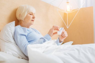 Yatakta kalırken bir makinelinin tutan yaşlı kadın konsantre