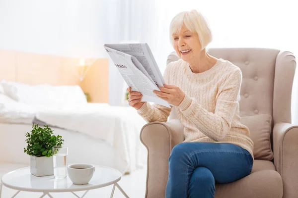 Щаслива старша жінка читає чудову статтю в газеті і посміхається — стокове фото