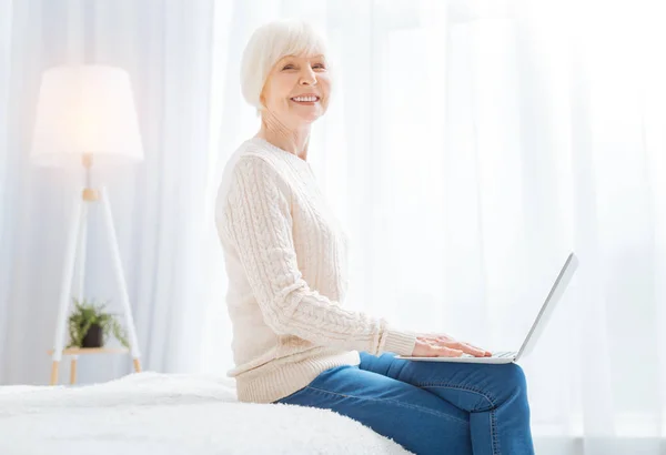 Emocionální veselý důchodce sedí s moderním zařízením a usmívá se — Stock fotografie