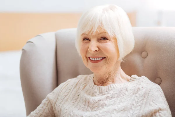 Очаровательная милая пожилая женщина чувствует себя счастливой, сидя и улыбаясь — стоковое фото