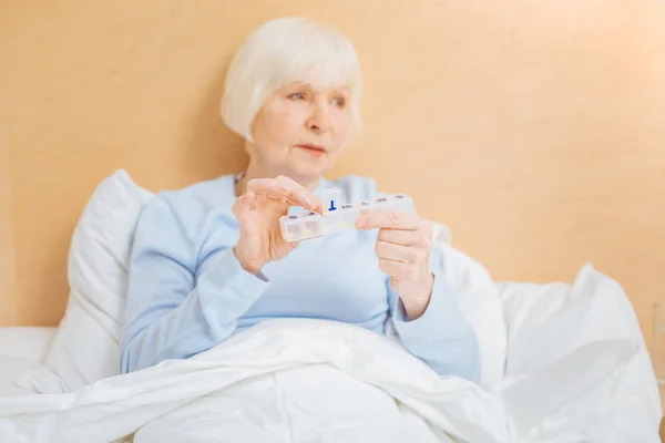 Enfermo anciano mujer sentado con su pillbox y mirando a la distancia — Foto de Stock