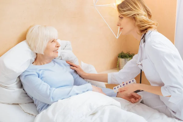 Amable médico responsable persuadiendo a su paciente mayor a quedarse en la cama — Foto de Stock