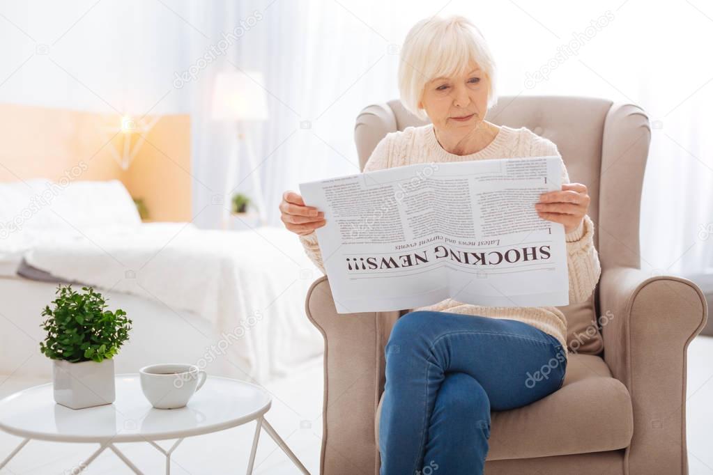 Smart aged person sitting at home and reading the newspaper