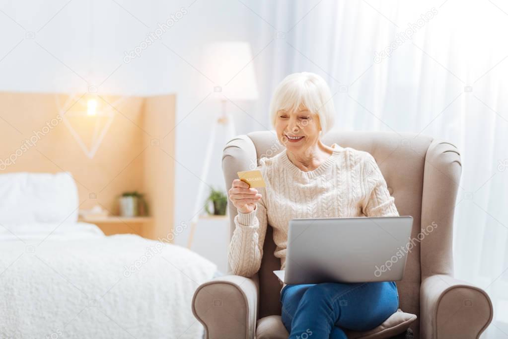 Pleasant aged woman sitting and smiling while looking at the card