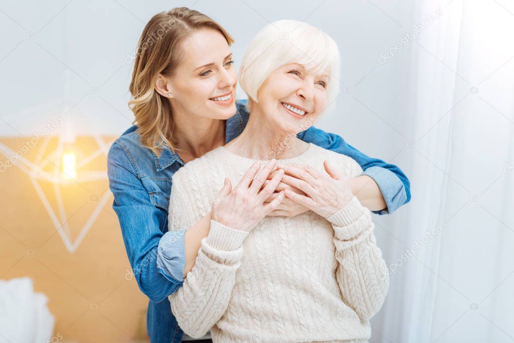 Kind attentive woman hugging her grandmother and smiling cheerfully