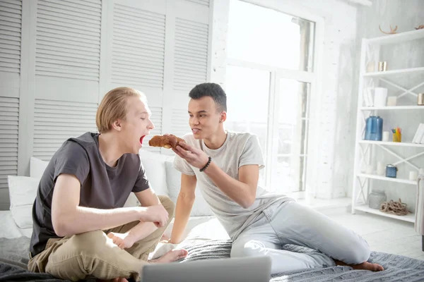 Funny gay couple eating croissant — Stock Photo, Image