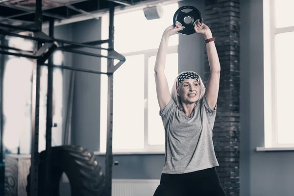 Energetic senior woman lifting up a weight disc