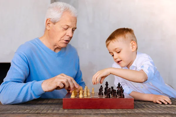 Przyjemny w wieku człowiek gra w szachy z jego wnuk — Zdjęcie stockowe