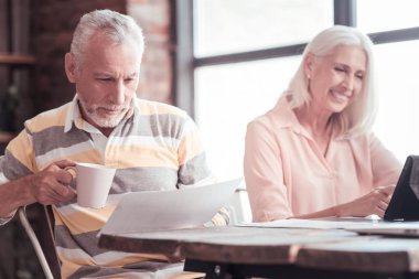 Bir fincan tutarak ve belgeyi okuyan ciddi meşgul adam.