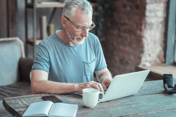 Hombre serio con gafas sentado y trabajando con el portátil . — Foto de Stock