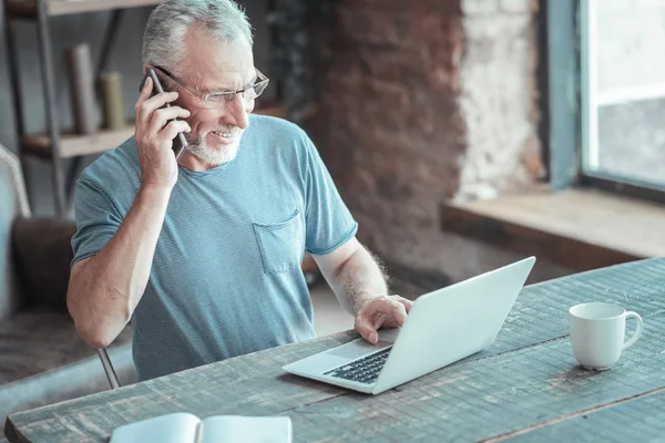 Vriendelijke senior man met behulp van de laptop en telefoon gesprek. — Stockfoto