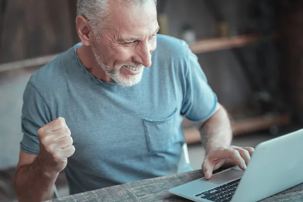 Задоволений приємний чоловік радіє і використовує ноутбук . — стокове фото